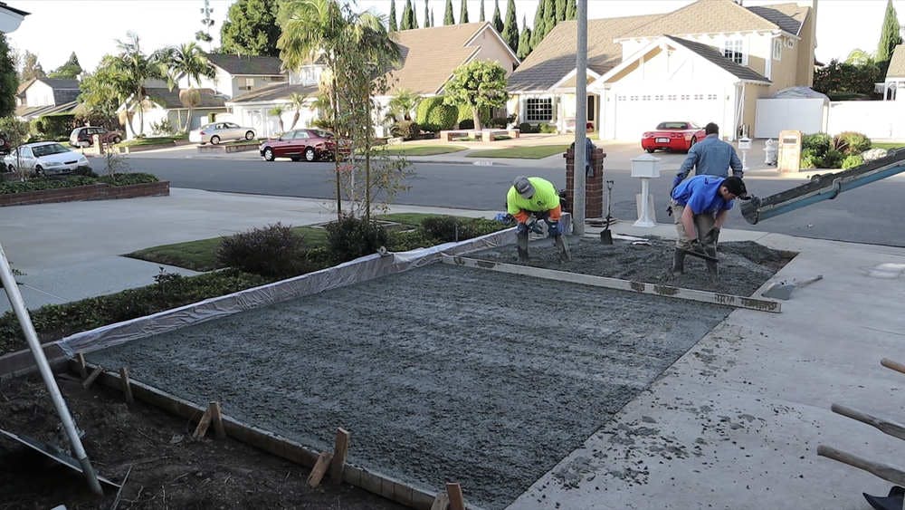 Concrete workers installing an addition to a concrete driveway.