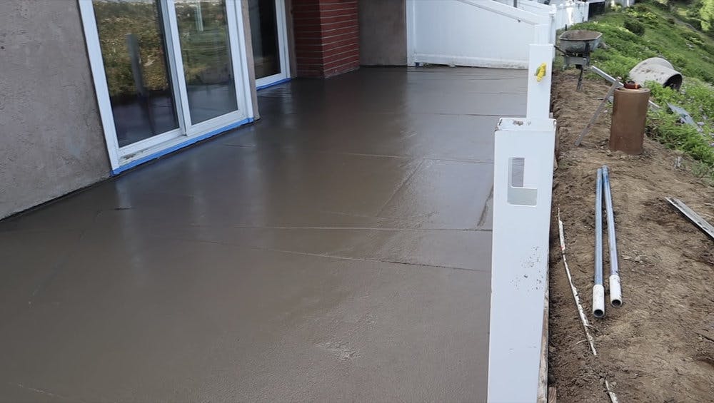 Wet concrete patio in backyard leading to a downsloped hill.