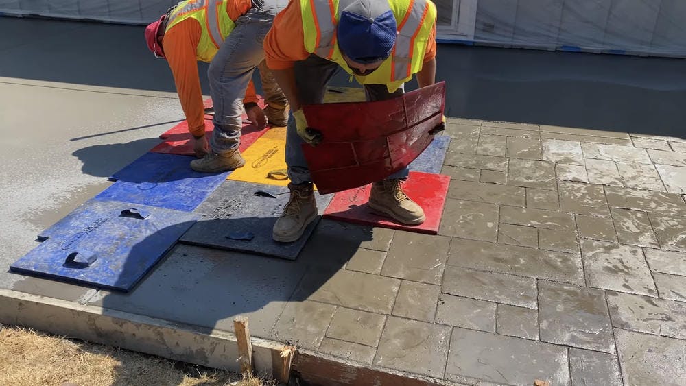 Two men applying stamps to concrete patio.
